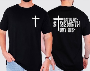 May include: Black t-shirt with a white cross on the front and the phrase "NOT BY MY STRENGTH BUT HIS" on the back. The shirt is a crew neck style and appears to be made of a soft material.
