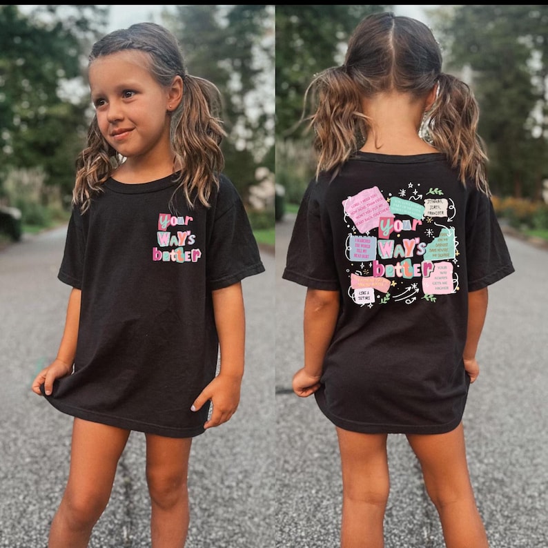 May include: Black t-shirt with the text "Your Way's Better" in colorful bubble letters on the front and back. The back of the shirt has additional colorful text and graphics. The shirt is worn by a young person with pigtails.