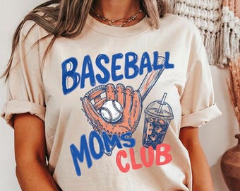Peut inclure: T-shirt beige avec l'inscription "BASEBALL MOMS CLUB" en bleu et rouge. Le motif comprend une balle de baseball, un gant et une boisson avec de la glace. Le t-shirt a des manches retroussées.