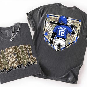 May include: Two gray t-shirts. One shirt has "Baseball Mama" in a camouflage design. The other shirt features a baseball player in a blue uniform with the name "James" and the number "12" on the back, holding a bat.