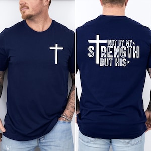 May include: Navy blue t-shirt with a white cross on the front and the text "NOT BY MY STRENGTH BUT HIS" on the back. The shirt is a crew neck style.