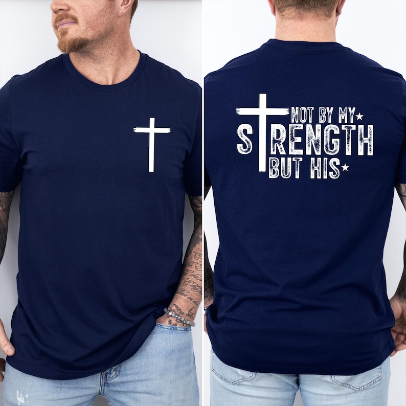 May include: Navy blue t-shirt with a white cross on the front and the text "NOT BY MY STRENGTH BUT HIS" on the back. The shirt is a crew neck style.