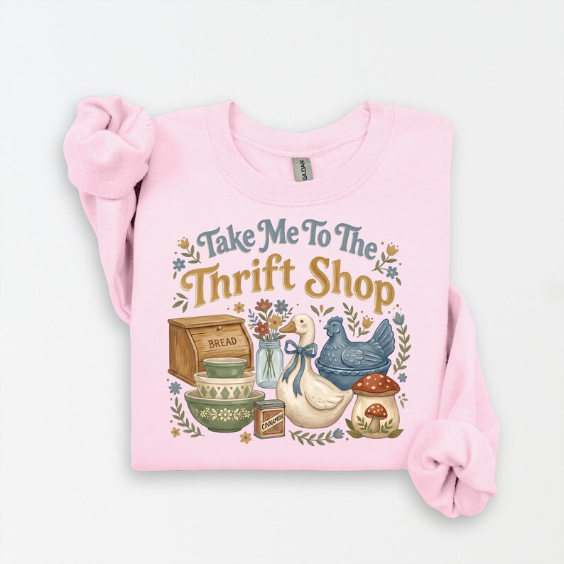 May include: A light pink sweatshirt with the phrase "Take Me To The Thrift Shop" in a whimsical font. The design includes illustrations of a duck, chicken, bowls, bread box, and mushrooms.