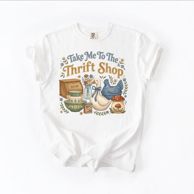 May include: White t-shirt with a colorful graphic that reads "Take Me To The Thrift Shop." The design features a bread box, bowls, a duck, a chicken, a mushroom, and other vintage-style elements.
