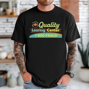 May include: Black t-shirt with the text "Quality Learning Center" in green and brown, and the phone number "1-800-FRAUD" in blue and yellow. The shirt is worn by a person with tattoos on their arm.