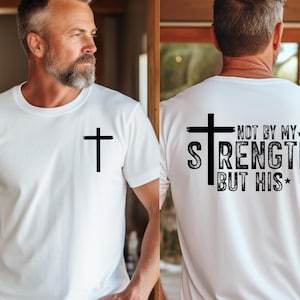 Men’s Christian tee featuring a small front cross and a large back design with a cross and the phrase “Not by my strength but His.” A clean faith-based style emphasizing strength through Christ.