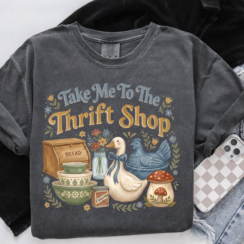Vintage-style drawing of a wooden bread bin, stacked bowls, and a white goose with a blue ribbon. The design features the phrase Take Me To The Thrift Shop in bold, nostalgic typography with earthy tones.