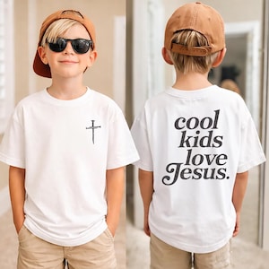 May include: White t-shirt with a black cross graphic on the front and the text "cool kids love Jesus" on the back. The shirt is worn with a brown baseball cap and sunglasses. The shirt is made of a soft, comfortable material.