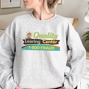 May include: A light gray sweatshirt with the words "Quality Learing Center" in green and brown, and the phone number "1-800-FRAUD" in yellow and blue. The sweatshirt has long sleeves.
