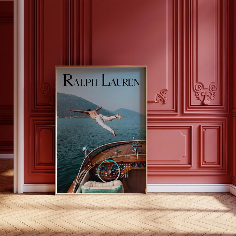 May include: A framed print featuring the text "Ralph Lauren" at the top. The image shows a person diving off a wooden boat into a body of water, with mountains in the background. The boat's steering wheel and dashboard are visible.