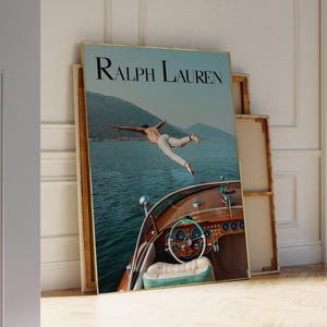 May include: A framed poster featuring the text "Ralph Lauren" at the top. The image shows a person mid-air, diving into the water from a wooden boat. The boat's interior is visible, with a steering wheel and seating.