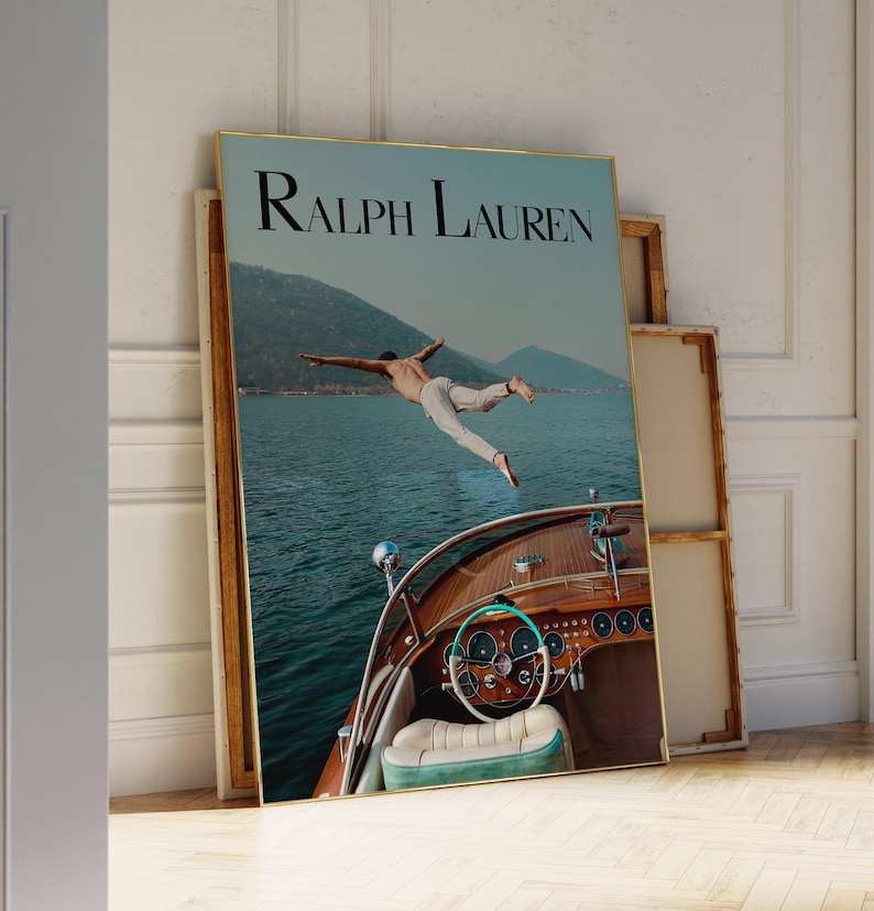 May include: A framed poster featuring the text "Ralph Lauren" at the top. The image shows a person mid-air, diving into the water from a wooden boat. The boat's interior is visible, with a steering wheel and seating.