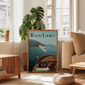 May include: A framed print featuring the text "Ralph Lauren" at the top. The image shows a person diving off a wooden boat into the ocean. The boat's dashboard and steering wheel are visible. The background includes mountains and water.