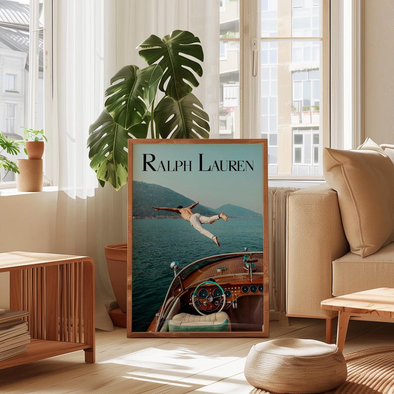 May include: A framed print featuring the text "Ralph Lauren" at the top. The image shows a person diving off a wooden boat into the ocean. The boat's dashboard and steering wheel are visible. The background includes mountains and water.