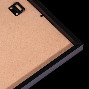 May include: A black picture frame with a brown backing and a metal hanger. The frame has a simple, modern design and is set against a black background.