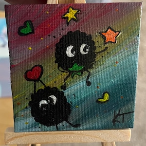 May include: Small acrylic painting on canvas depicting two black, fluffy characters with large white eyes and green details. The background fades from red to blue, with stars and hearts. Signed "KT".