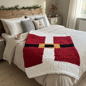 May include: A chunky knit throw blanket featuring a Santa Claus suit design with a red body, a wide white vertical stripe, a black horizontal belt, and a gold-coloured square buckle. The blanket is made of thick, soft yarn with a visible textured stitch.