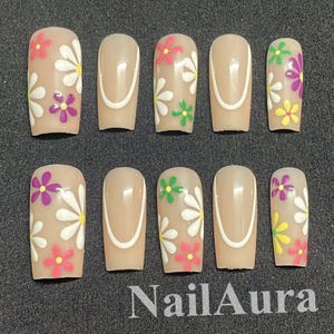 Könnte beinhalten: Ein Set aus zehn künstlichen Nägeln in einem neutralen Beigeton. Einige Nägel weisen ein weißes, geschwungenes Design auf, während andere mit bunten Gänseblümchenmustern in Rosa, Lila, Grün und Gelb verziert sind.