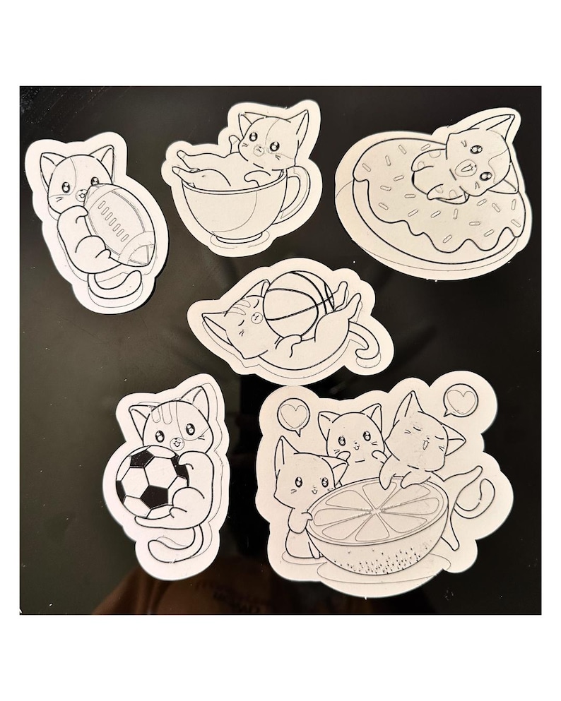 Puede incluir: Una colecci&oacute;n de seis pegatinas troqueladas en blanco y negro con gatos de dibujos animados. Los dise&ntilde;os incluyen un gato con un bal&oacute;n de f&uacute;tbol americano, en una taza, sobre un d&oacute;nut, con un bal&oacute;n de baloncesto, un bal&oacute;n de f&uacute;tbol y una fruta c&iacute;trica.