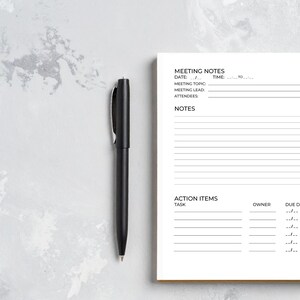 May include: A black pen rests beside a spiral-bound notebook with meeting notes. The notebook's pages are white, with lines for notes, action items, and due dates. The text "MEETING NOTES" is visible at the top.