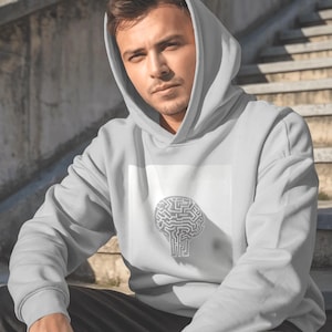 May include: A light gray hoodie with a white square graphic featuring a brain-shaped maze design. The hoodie has a hood and long sleeves. The person is sitting on concrete steps.
