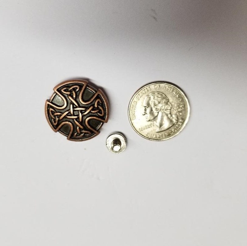 May include: A copper-colored metal button with a Celtic cross design. The button is about the size of a US quarter.