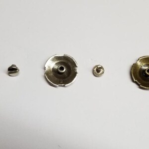 May include: Three sets of metal fasteners, each with a round, decorative top and a screw. The tops are copper, silver, and gold in color.