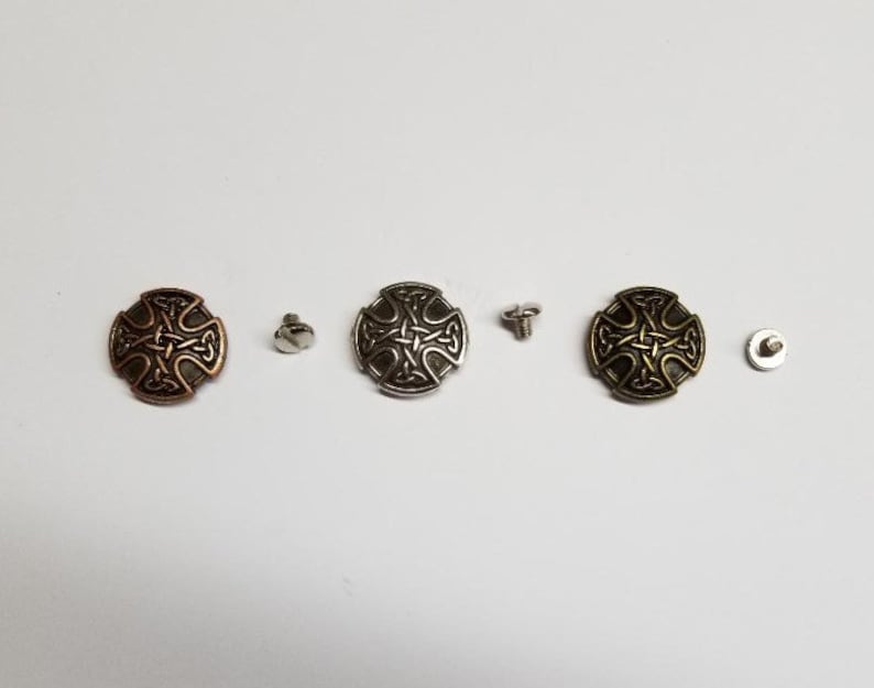 May include: Three metal Celtic cross-shaped buttons with a black design. The buttons are in copper, silver, and gold tones. Each button comes with a screw for attaching.