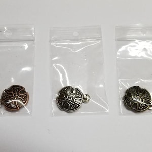 May include: Three small, round, metal charms with a Celtic knot design. The charms are in three different finishes: copper, silver, and gold.