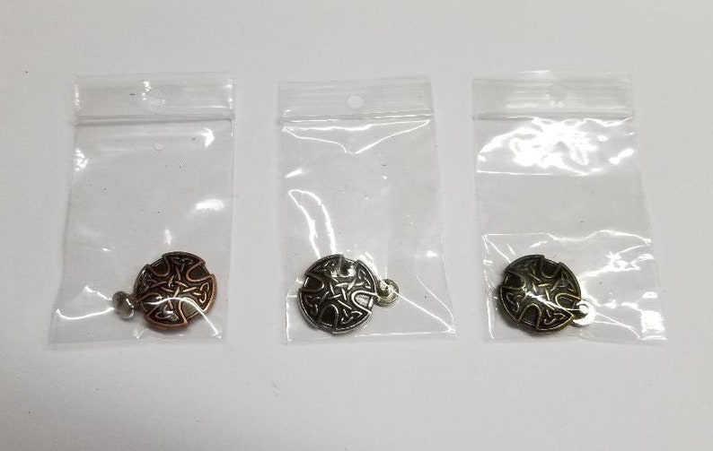 May include: Three small, round, metal charms with a Celtic knot design. The charms are in three different finishes: copper, silver, and gold.
