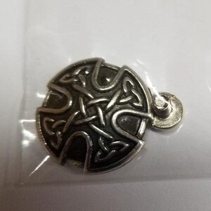 May include: A silver Celtic knot pendant with a black background. The pendant is round and has a loop at the top for attaching to a chain.