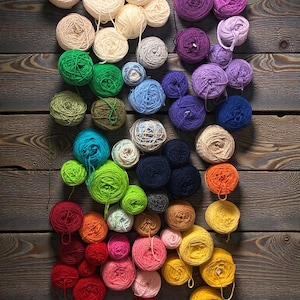 May include: A collection of colorful yarn balls arranged on a wooden surface. The yarn balls are in various colors, including green, blue, purple, yellow, and red. The wooden surface has a weathered appearance.