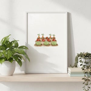 Könnte beinhalten: Ein gerahmter Aquarelldruck mit einer Gartenszene mit Karotten, Tomaten und Salat. Das Kunstwerk wird auf einem hellen Holzregal ausgestellt, mit einer Topfpflanze links und einer kleinen Sukkulente rechts.
