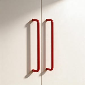 May include: Two bright red, tubular door handles are mounted on a white cabinet. The handles are straight with curved ends, casting long shadows. The minimalist design offers a modern aesthetic.