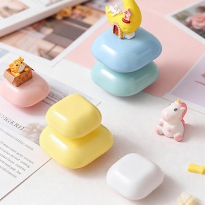 May include: A collection of colorful, miniature decorative objects. Includes a stack of blue and green stones topped with a yellow crescent moon and house, a pink stone with a tiger, a yellow stone stack, a white stone, and a small unicorn figurine.