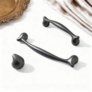 May include: A set of three matte black cabinet hardware pieces. The set includes two curved bar pulls and a single knob. The hardware has a smooth, modern design, suitable for drawers and cabinets.