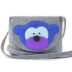 May include: A gray felt crossbody bag with a blue felt monkey face appliqué. The monkey has purple, blue, and white felt details.