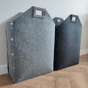 Puede incluir: Dos contenedores de almacenamiento de fieltro gris con forma de casa. Cada uno tiene una abertura rectangular para el asa y botones decorativos. Uno es gris claro, el otro gris oscuro.