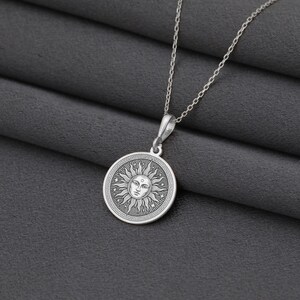 A silver necklace with a circular pendant featuring a sun design.