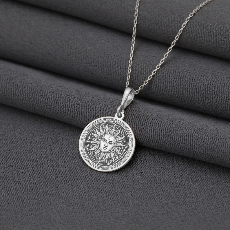 A silver necklace with a circular pendant featuring a sun design.