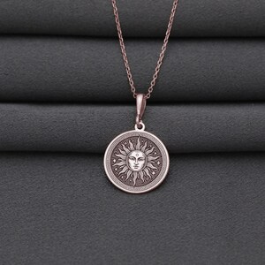 A silver-colored pendant necklace with a circular medallion featuring a sun design.
