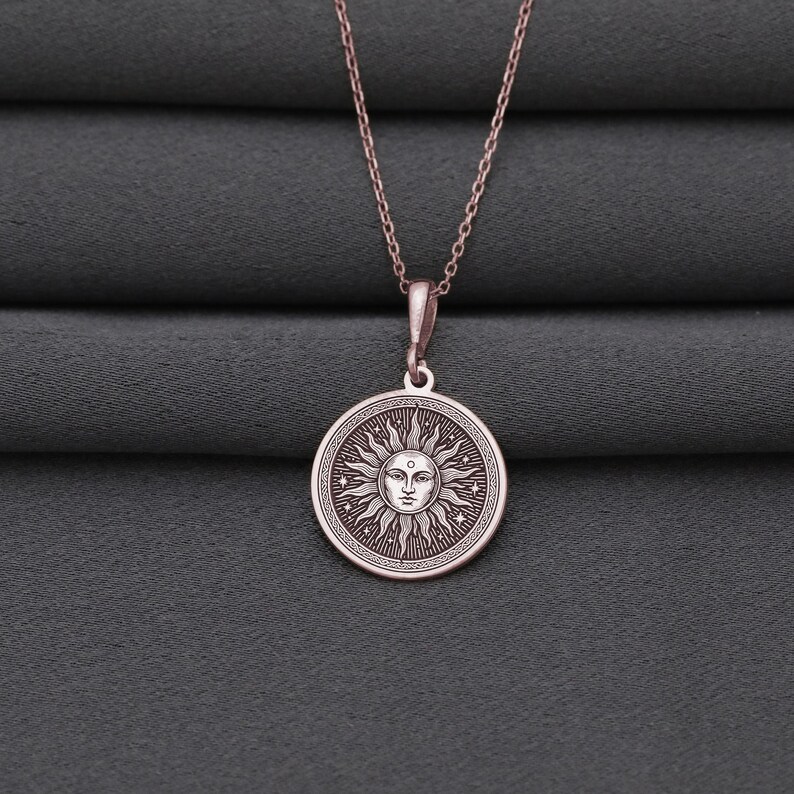 A silver-colored pendant necklace with a circular medallion featuring a sun design.