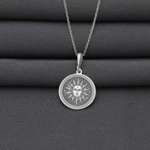 A silver necklace with a circular pendant featuring a sun design.