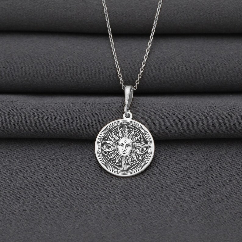 A silver necklace with a circular pendant featuring a sun design.
