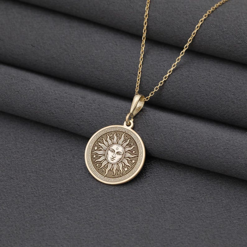 A gold-colored necklace with a circular pendant featuring a sun design.