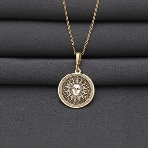 A gold-colored necklace with a circular pendant featuring a sun design.