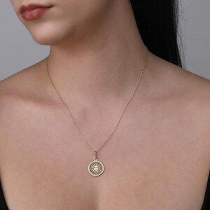A close-up of a woman's neck and chest area wearing a gold necklace with a circular pendant.