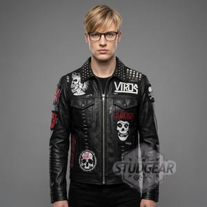Pode incluir: Jaqueta de couro preta com vários patches com gráficos de caveiras e a palavra "Virus". A jaqueta tem gola com tachas e fecho de zíper. A jaqueta é um estilo punk rock clássico.