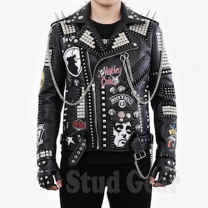 May include: Black leather jacket adorned with silver studs and spikes. The jacket displays various patches, including "Mötley Crüe" and "Rock n' Roll" motifs. It features a chain detail and matching studded gloves. A striking, edgy fashion item.