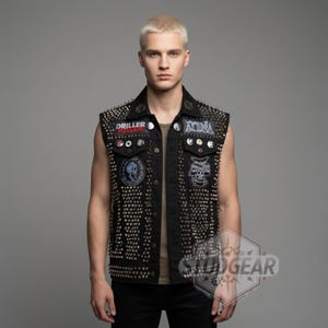 May include: Black denim vest heavily embellished with silver studs and patches. The vest features a button-up front, a collar, and multiple patches with graphic designs and text. A bold fashion statement.